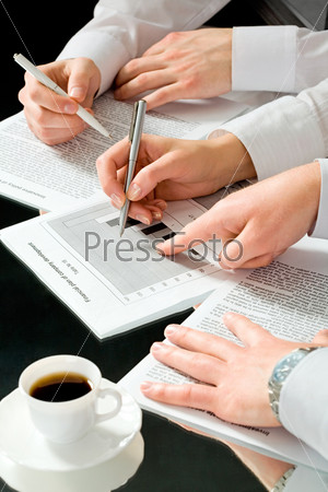 Image of business people’s hands during discussion of business documents with a cup of coffee near by
