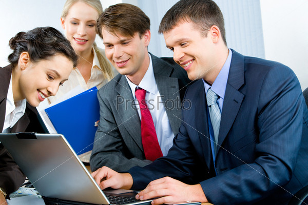 Four business persons gathered together looking at monitor of laptop