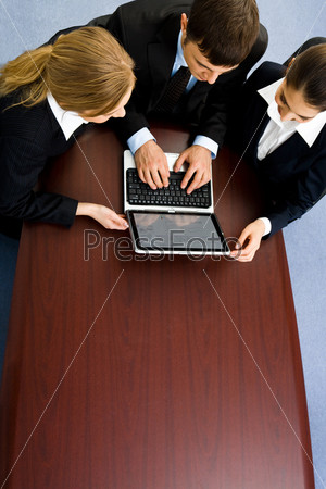 Business team of three people gathered together round the large wood table  and working