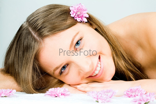Photo of a young happy woman lying in the spa salon and enjoying herself with some flowers at the front