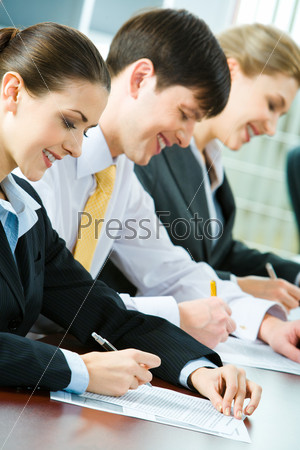 Three business people sitting at the table writing and smiling