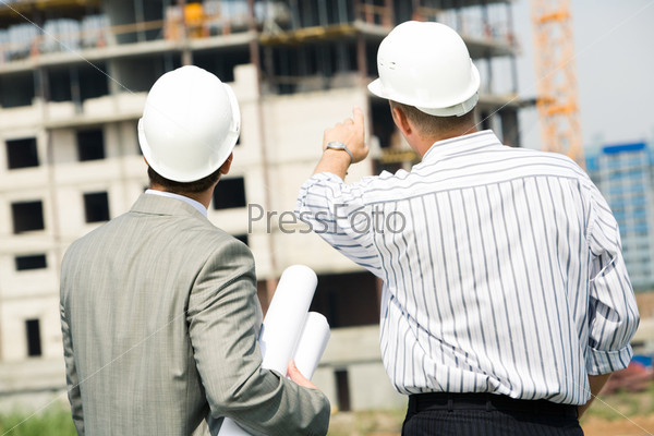 Portrait of boss pointing at construction with worker near by