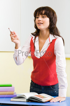 Portrait of confident teacher standing at her desk with open textbook on it