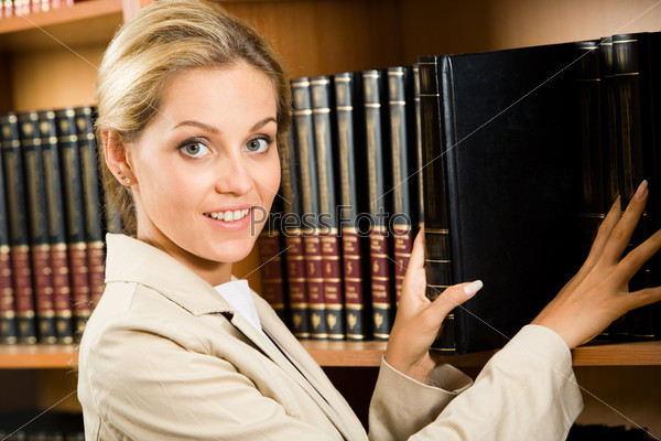 Portrait of business lady touching books that stand on shelf and looking at camera