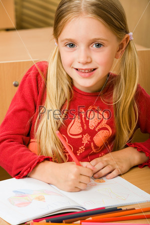Portrait of schoolgirl drawing in her copybook during lesson and looking at camera