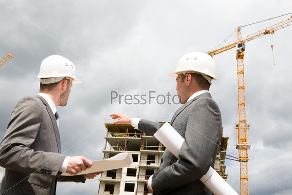 Photo of young engineer showing something to his partner at building site, stock photo