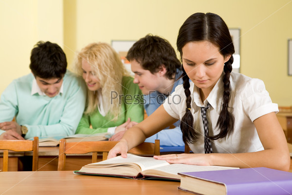 Portrait of serious students sitting at their tables and reading textbooks with smart girl at foreground