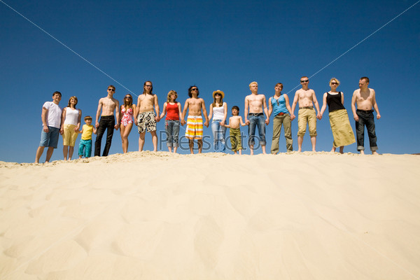 Image of many friends standing on sandy beach holding by hands