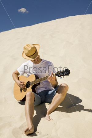 Portrait of happy man in cowboy hat playing the guitar on sandy beach