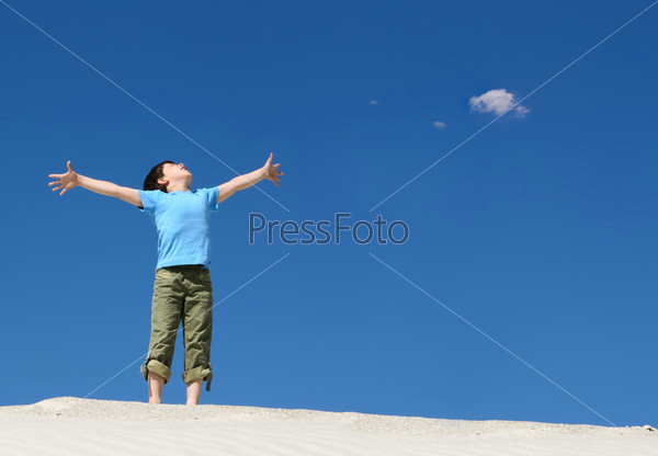 Image of joyful boy in casual clothes standing on sand with his arms outstretched