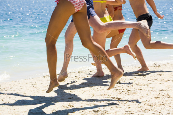 Legs of friends on sandy beach going to run into water