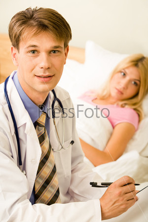 Portrait of handsome doctor looking at camera on background of his patient