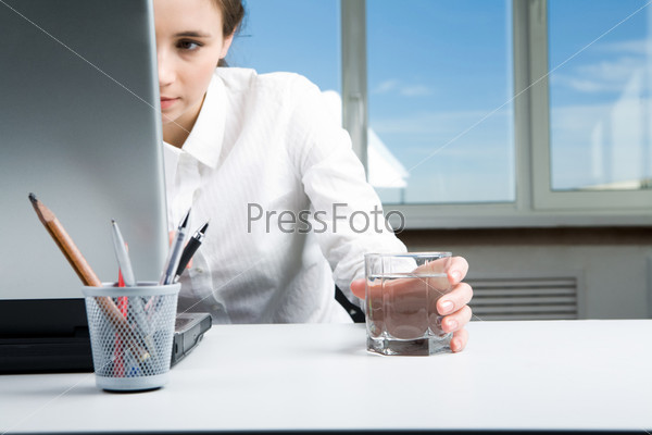 Image of executive female looking into laptop display and keeping hand on glass of water in office
