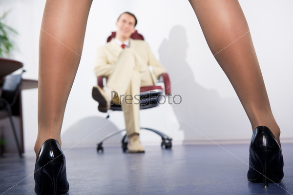 Photo of feminine legs in high heeled shoes with sitting businessman at background