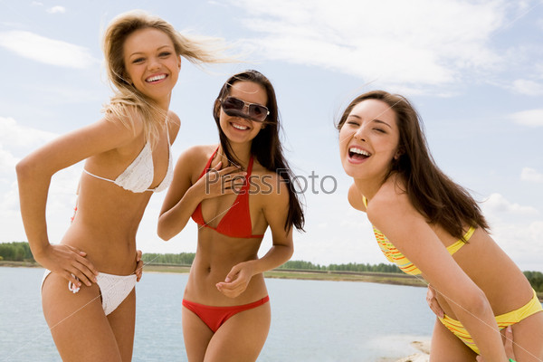 Portrait of three slim girlfriends in bikini laughing at camera on hot summer day