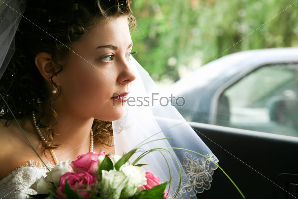 Face of bride looking from the car window with bunch of white and pink roses
