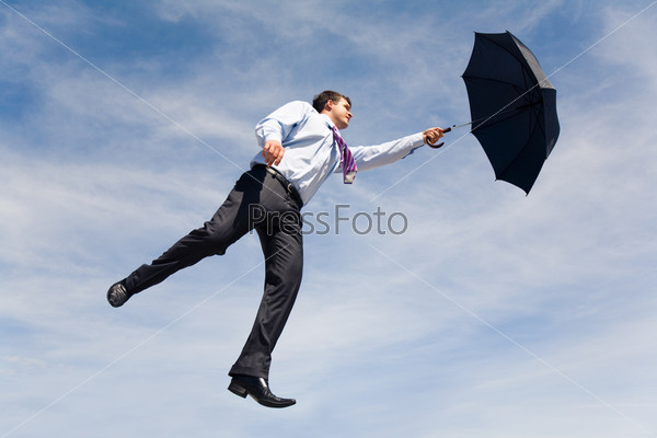 Conceptual photo of businessman flying on his umbrella up into bright blue sky