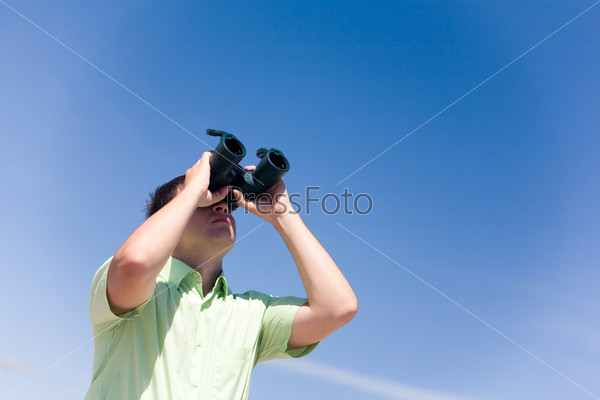 Portrait of serious businessman looking through binoculars on the background of blue sky