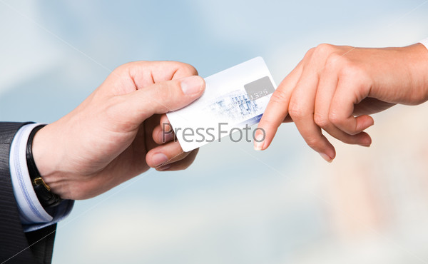 Close-up of transfer of credit card from maleâ??s hand to that of female over blue background