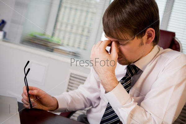 Photo of fatigue man with his eyeglasses off keeping his hand near face after hard working day