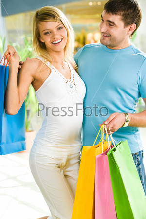 Photo of happy man and woman standing together and carring shopping bags in the shop