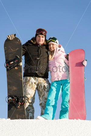 Portrait of successful skiers with boards in hands over blue sky