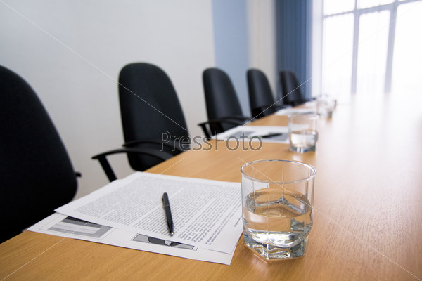 Image of glass of water on workplace with paper, pen and armchairs near by