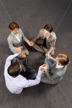 Above view of business people sitting on the floor and holding each other by hands