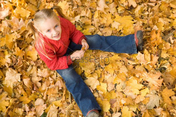 Above view of smiling girl sitting on autumnal ground and looking at camera