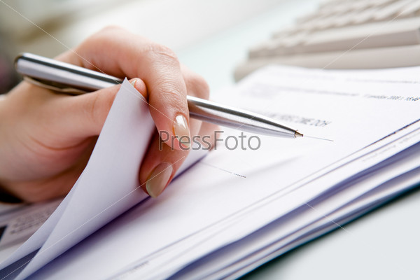 Close-up of  hand holding pen with paper over pile of documents