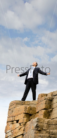 Vertical image of lucky businessman standing on the top of mount and looking upwards with his arms outstretched