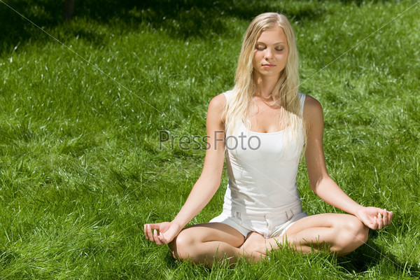 Image of meditating girl seated in pose of lotus on green grass