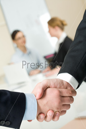 Photo of handshake of businessmen on background of communicating co-workers