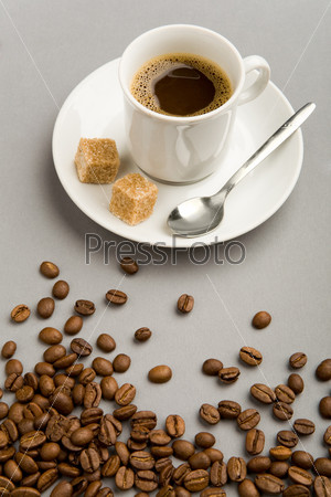 Photo of cup of black coffee with two pieces of sugar and brown beans near by