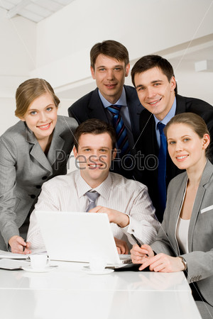 Portrait of several successful co-workers looking at camera with smiles at workplace