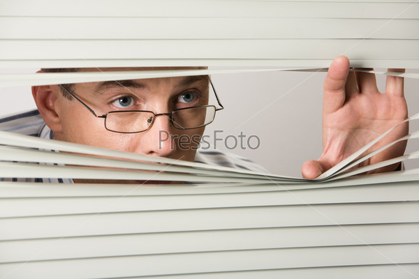 Close-up of businessman peeking out of Venetian blind