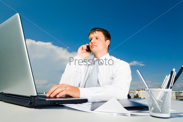 Portrait of confident businessman calling by mobile and typing on the laptop
