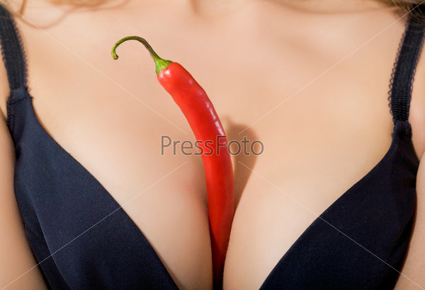 Red hot chili pepper between woman\'s breasts in black bra