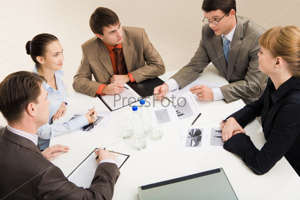 Group of five businesspeople discussing different questions gathered together around the table
