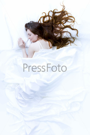 Above view of young beautiful woman sleeping in bed covered with white silky sheet