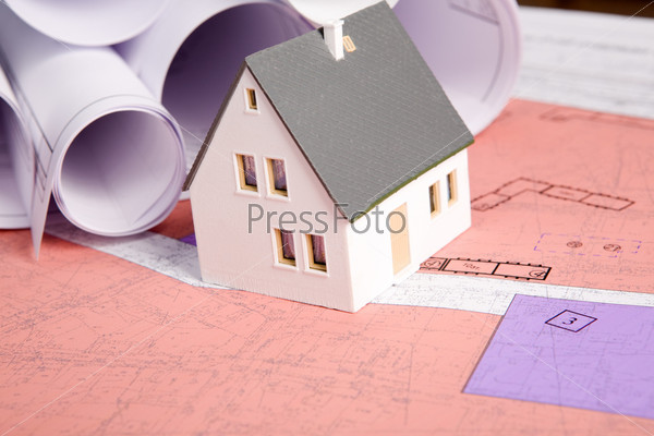 Close-up of toy house model with rolled blueprints near by