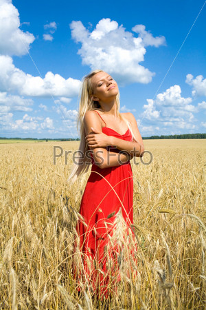 Photo of pretty blonde in red dress standing in wheat field and enjoying summer day