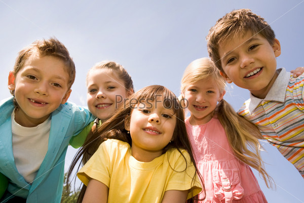 Portrait of smart preschoolers embracing each other on background blue sky