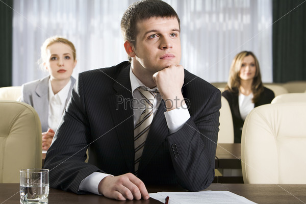 Portrait of boring man sitting at the table and two women on the background
