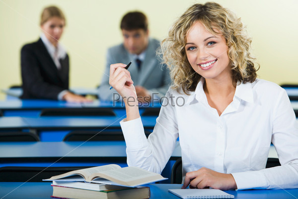 Portrait of smart student holding the pen and sitting at the table with books