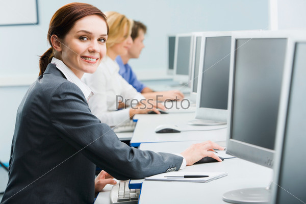 Portrait of busy woman sitting at the computer table and touching computer mouse on the background of businesspeople