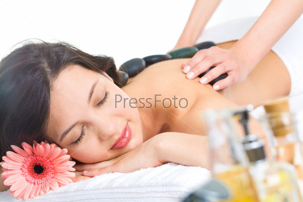 Photo of young naked woman getting a stone massage in a spa