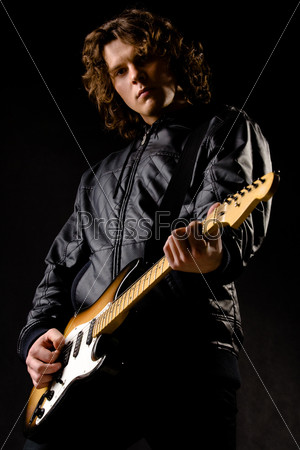 Portrait of young modern guitar player holding instrument in hands on black background