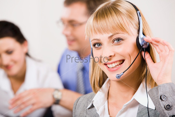 Attractive secretary with headset on the background of her coworkers