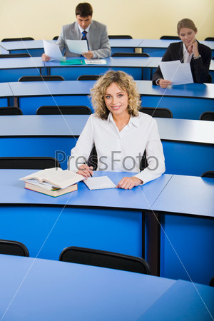 Portrait of smart woman sitting at the blue table with books on it in the classroom
